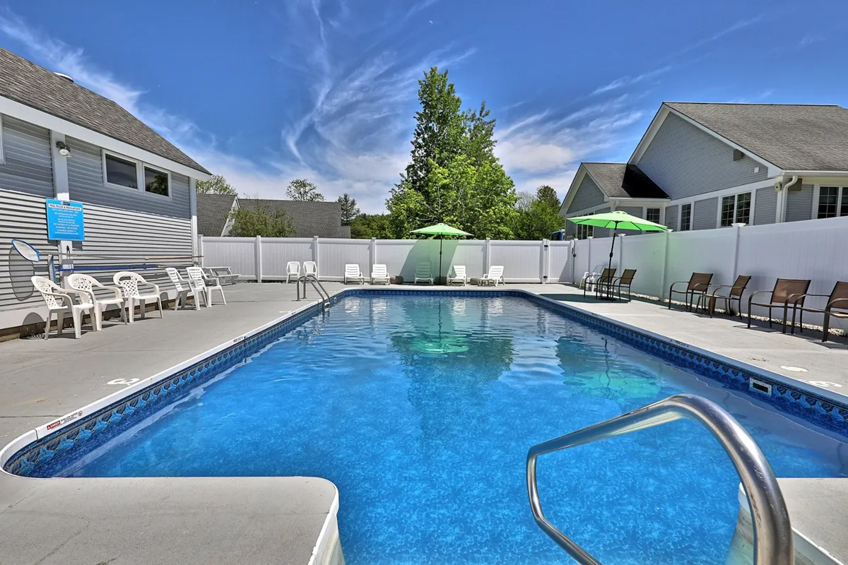 This image features an inviting outdoor heated swimming pool surrounded by lounge chairs, umbrellas, and lush greenery. The scene is bright and cheerful, with hints of social interaction and relaxation under the sun.