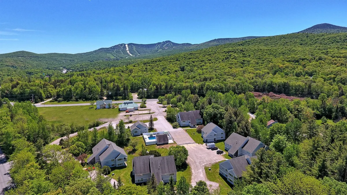 An exterior view capturing the swimming pool, a backdrop of majestic mountains, a lush tree canopy, and several buildings, suggesting the property's proximity to natural adventures and resort-style amenities.