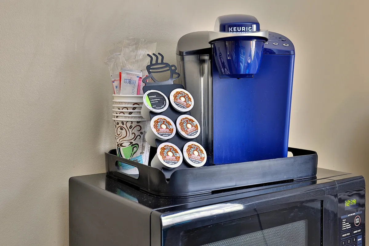 A close-up view of a Keurig coffee maker, a selection of coffee pods, cups, and napkins on a countertop. The setup evokes the aroma of fresh coffee and the promise of a relaxed morning routine.