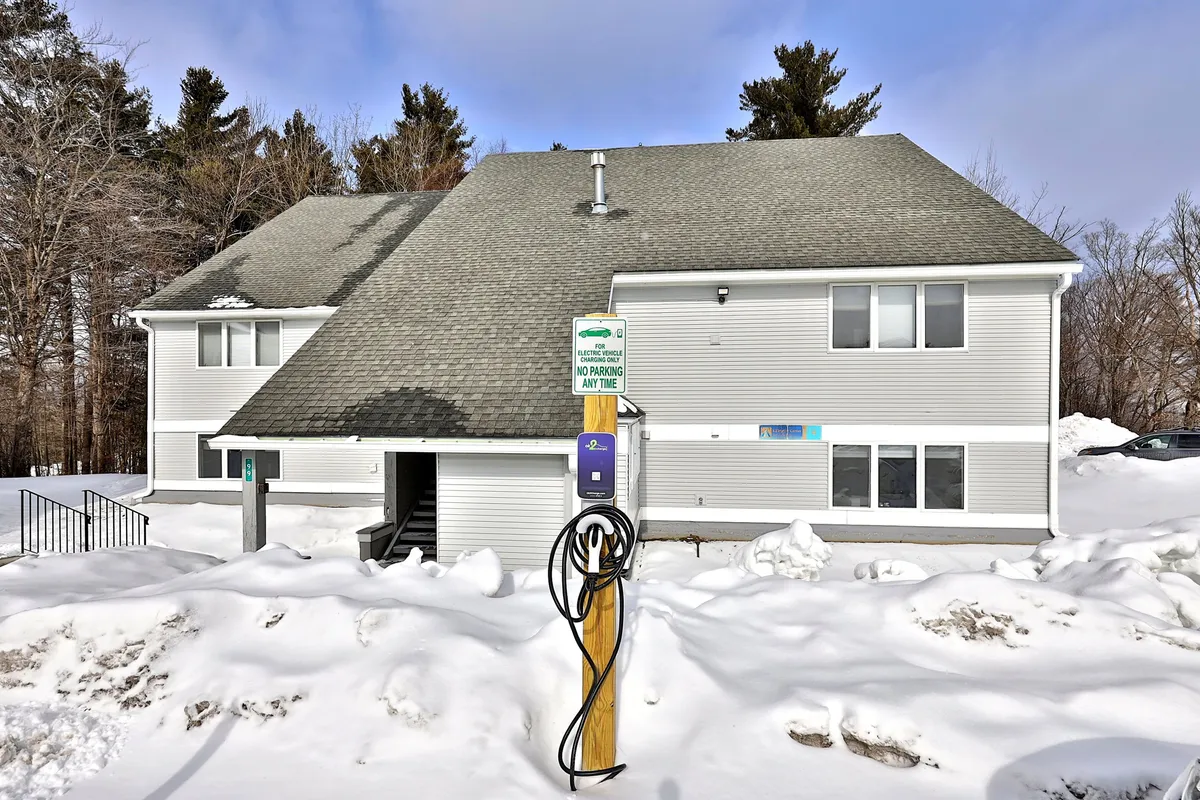 A snow-covered landscape frames the building's facade, with a parking meter in the foreground. The scene exudes winter serenity and hints at easy access for snowy-season activities.